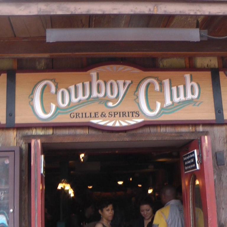 Die Fassade des Restaurants Cowboy Club mit einem großen Holzschild, das Grill & Spirits anbietet.
