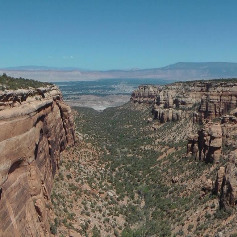 Ein weitwinkel-Panoramabild zeigt einen tiefen Canyon, dessen Seiten von felsigen Klippen und einer vegetationsbedeckten Ebene begrenzt werden.