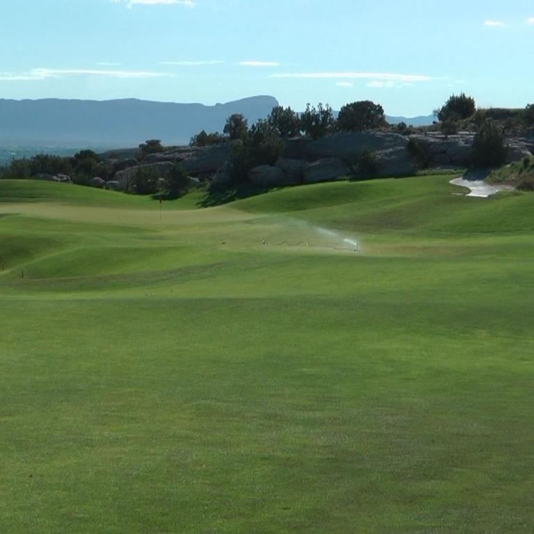 Panoramaaufnahme eines Golfplatzes mit weitläufigen Grüns und Blick auf eine Bergkette im Hintergrund.