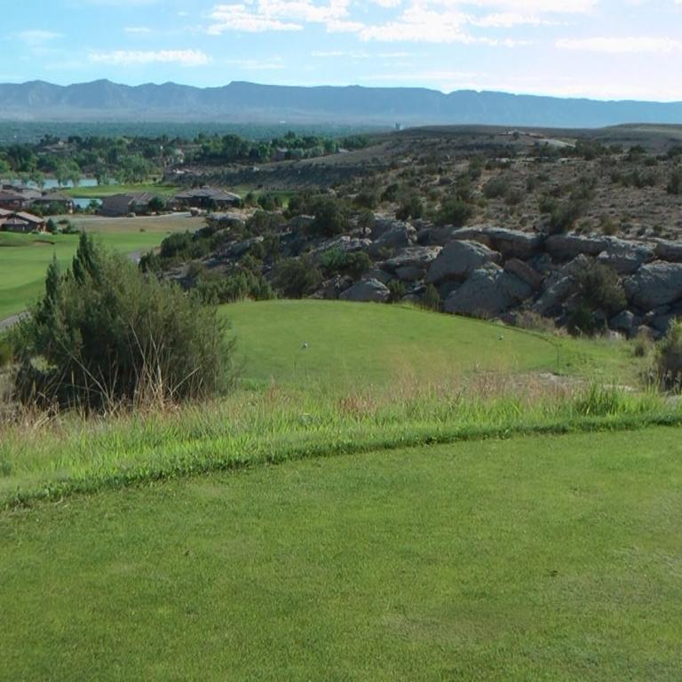 Panoramablick von einem Golfplatz, der sich durch eine weite, bergige Landschaft zieht.