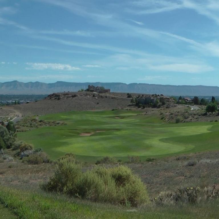 Weite Aufnahme eines Golfplatzes mit Blick auf eine Küstenlinie und Berge unter blauem Himmel