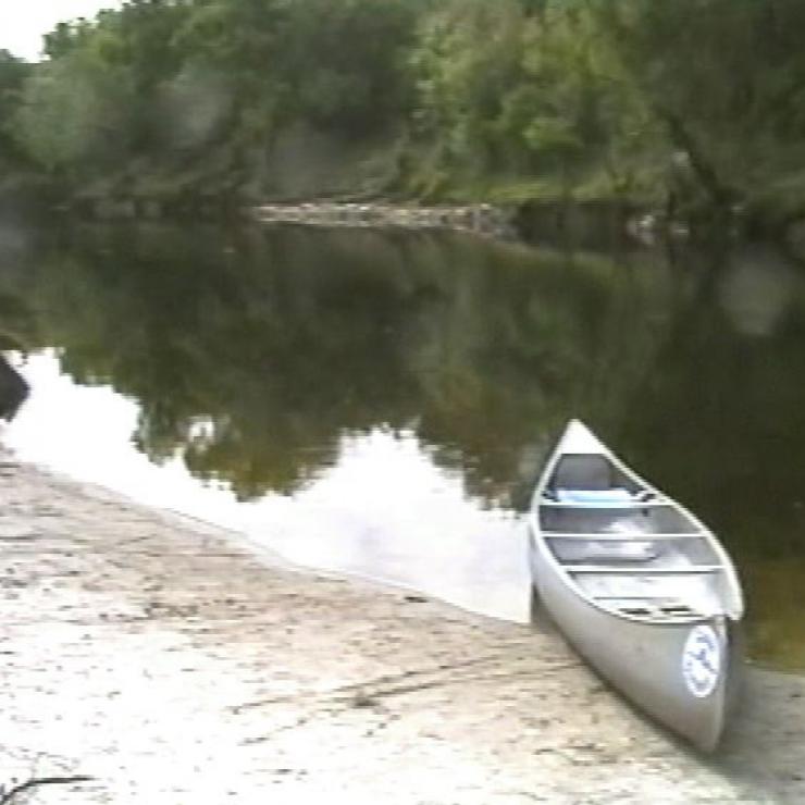 Ein kleines Boot steht an einem schlammigen Ufer eines ruhigen Flusses.