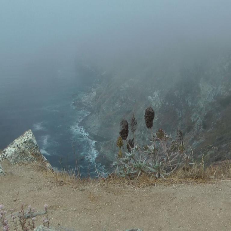Blick von einer trockenen Klippe über einen dichten Nebel auf ein Gewässer