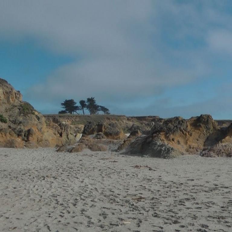 Küstenlandschaft mit steilen Klippen, einem Sandstrand und felsigen Formationen.