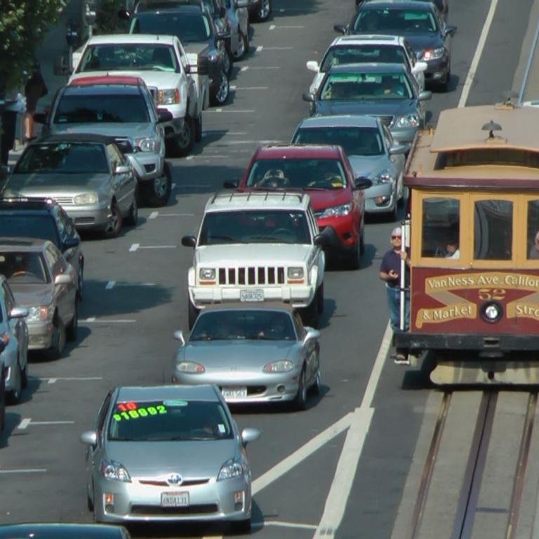 Eine Aufnahme von einem belebigten städtischen Verkehr, auf der mehrere moderne Autos und ein historischer Wagen zu sehen sind.