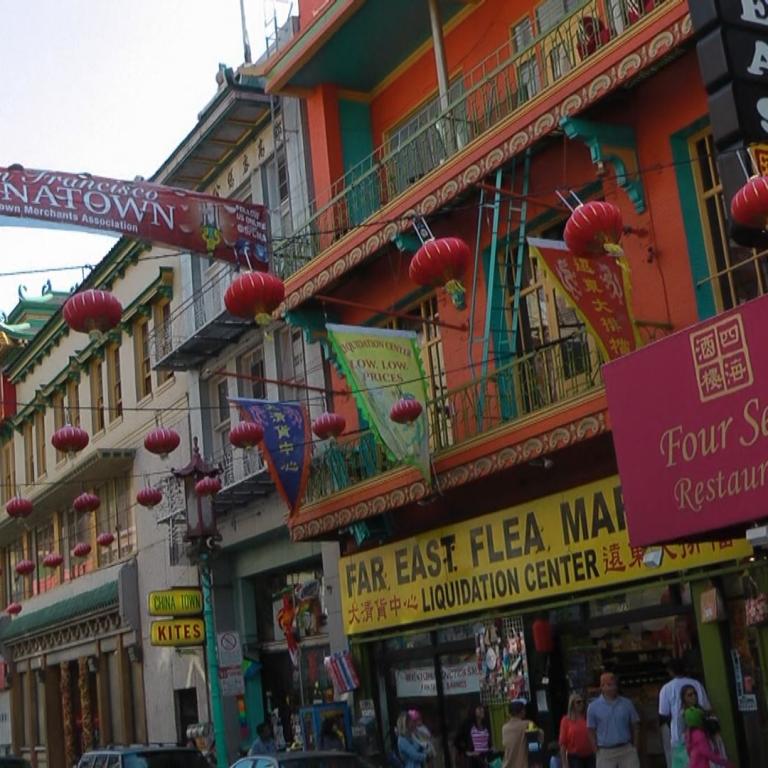 Eine farbenfrohe Straßenansicht in Chinatown, die belebte Geschäfte, einen Flohmarkt und ein asiatisch inspiriertes Restaurant zeigt.