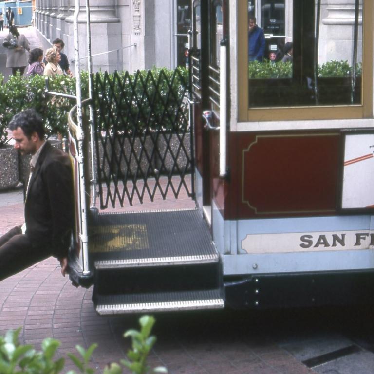Ein Mann in dunklem Anzug steht vor dem Einstieg eines historischen Stadtbusses oder Tram in einer städtischen Umgebung.