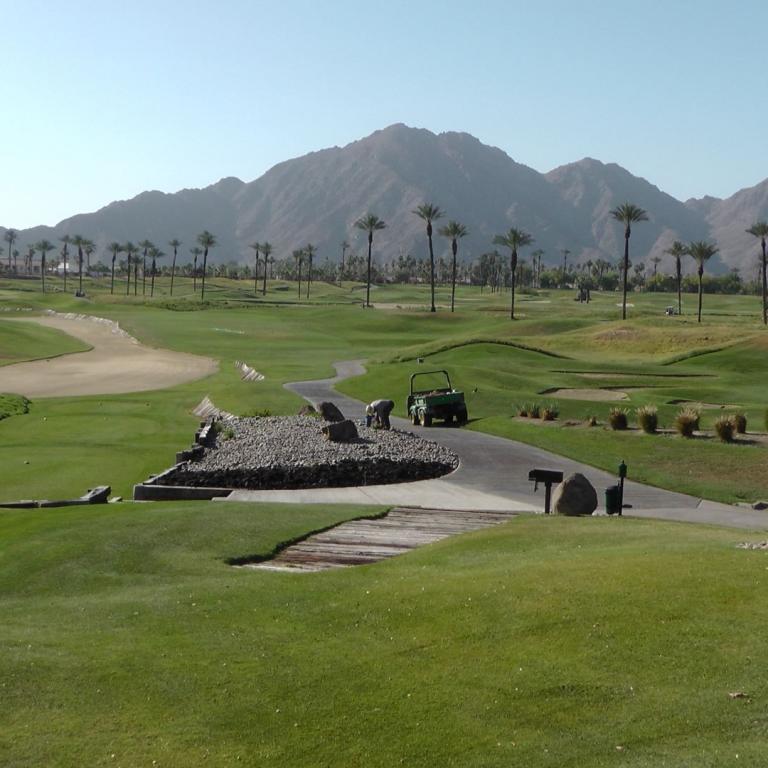 Ein weitläufiges Golfplatzpanorama mit gepflegtem grünem Rasen und majestätischen Bergen im Hintergrund.