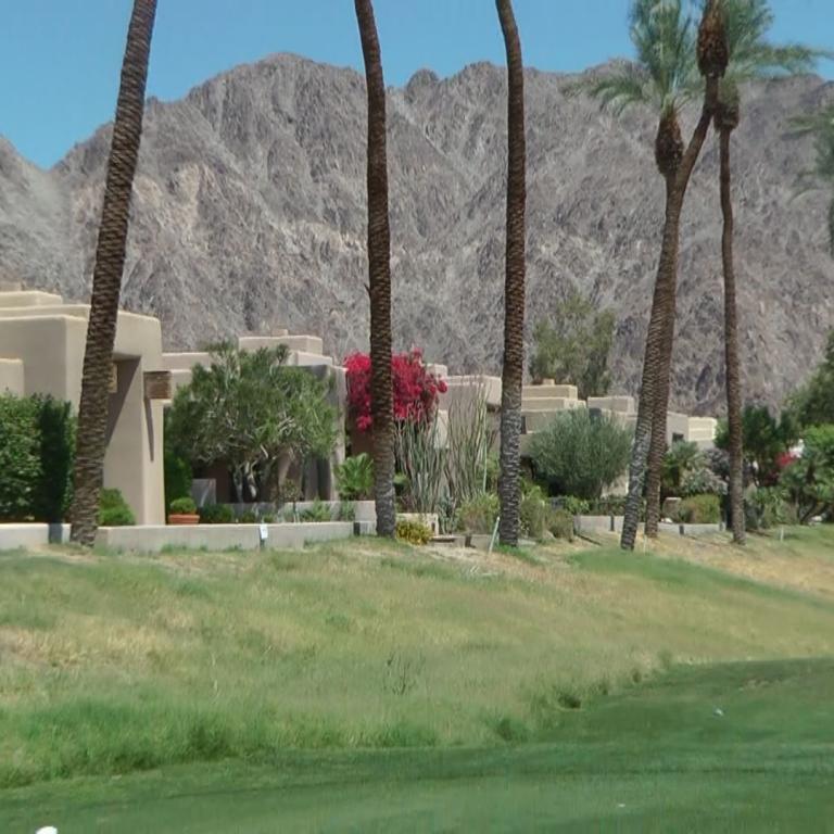 Ein Golfplatz mit Palmen und modernen Wohnhäusern vor einer beeindruckenden Bergkulisse.