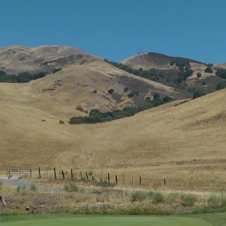 Weite, hügelige Landschaft mit sanften, braunen Kuppen unter blauem Himmel.