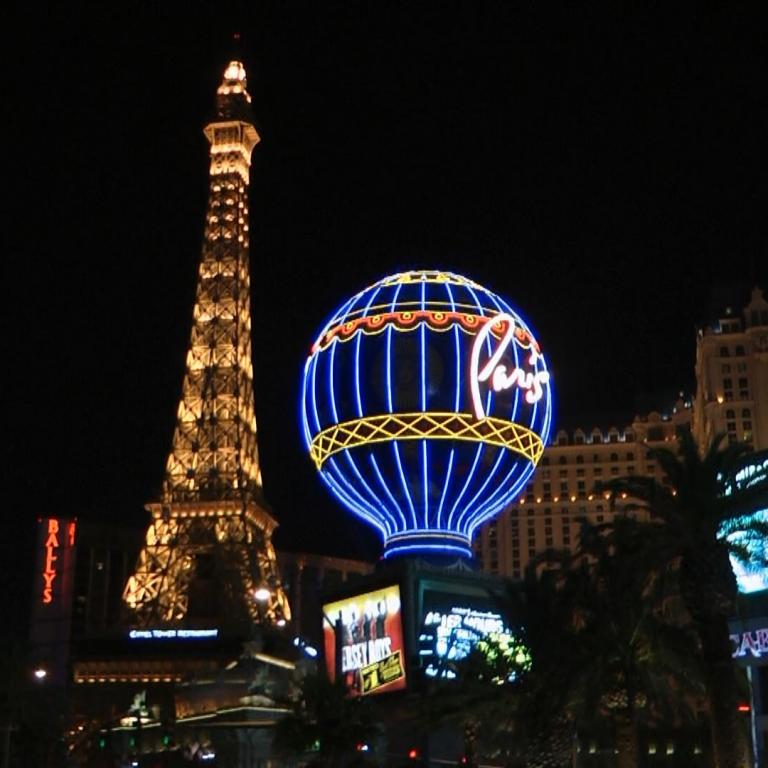 Die beleuchteten Wahrzeichen von Paris bei Nacht, bestehend aus dem Eiffelturm, einem blauen Ballon und modernen Gebäuden.