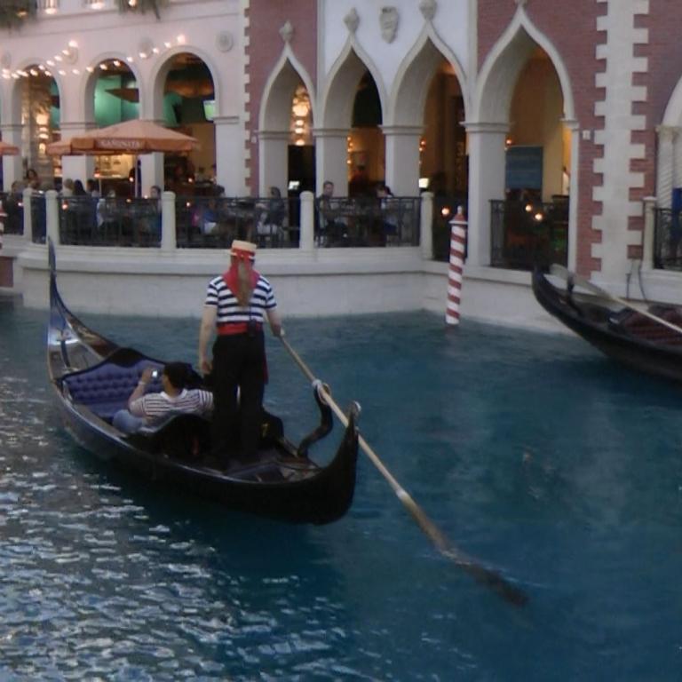 Ein Boot fährt auf einem Kanal durch eine städtische Geschäftszeile mit Arkaden.