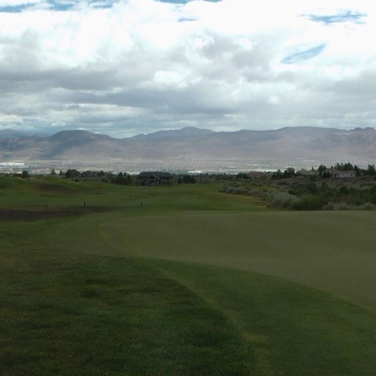 Panoramaaufnahme eines Golfplatzes mit Blick auf die Bergkette bei bewölktem Himmel.