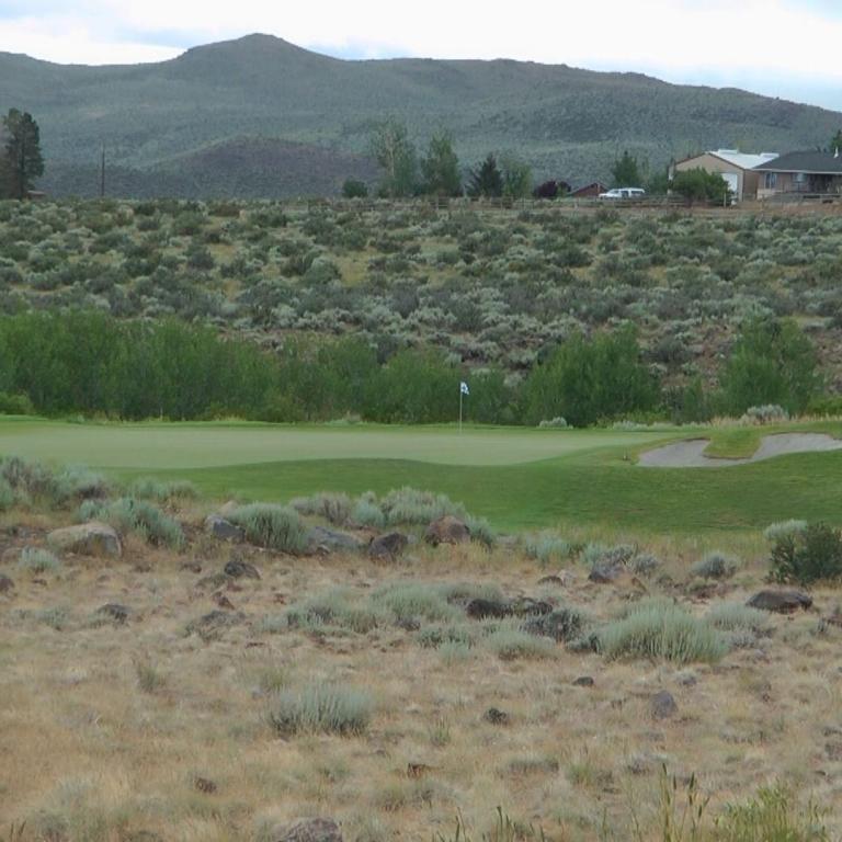 Eine Landschaftsaufnahme, die einen Golfplatz in einer trockenen Buschlandschaft vor dem Hintergrund von bewaldeten Bergen zeigt.