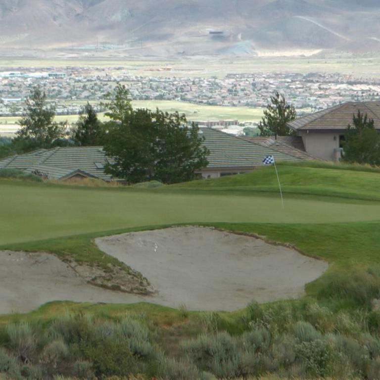 Panoramaaufnahme eines Golfplatzes mit einer weitläufigen Sicht auf eine Stadt und Berge im Hintergrund.