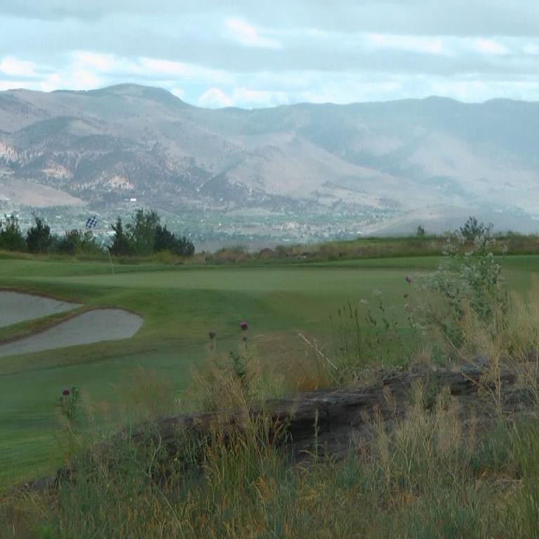 Panoramablick auf einen Golfplatz mit Blick auf eine große, dunstige Bergkette im Hintergrund.