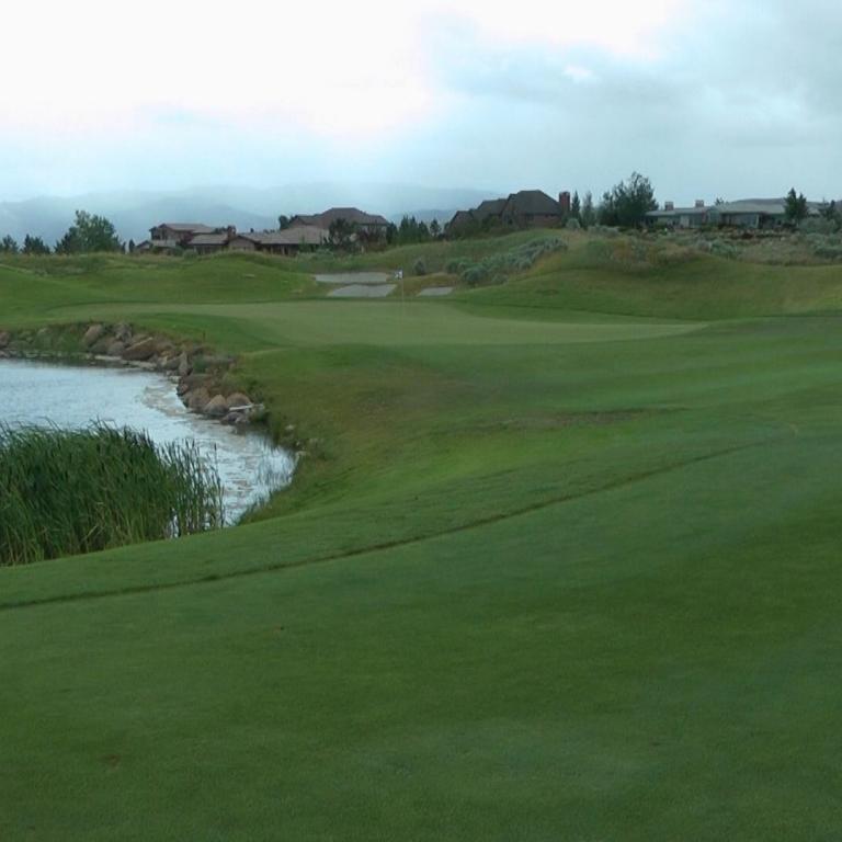 Eine weite Aufnahme eines Golfplatzes mit einem Teich im Vordergrund und Bebauung im Hintergrund unter bewölktem Himmel