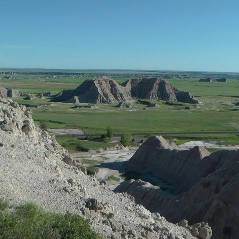 Ausgewachsene, erodierte Hügel und Strukturen in einer weiten, flachen Landschaft unter blauem Himmel.