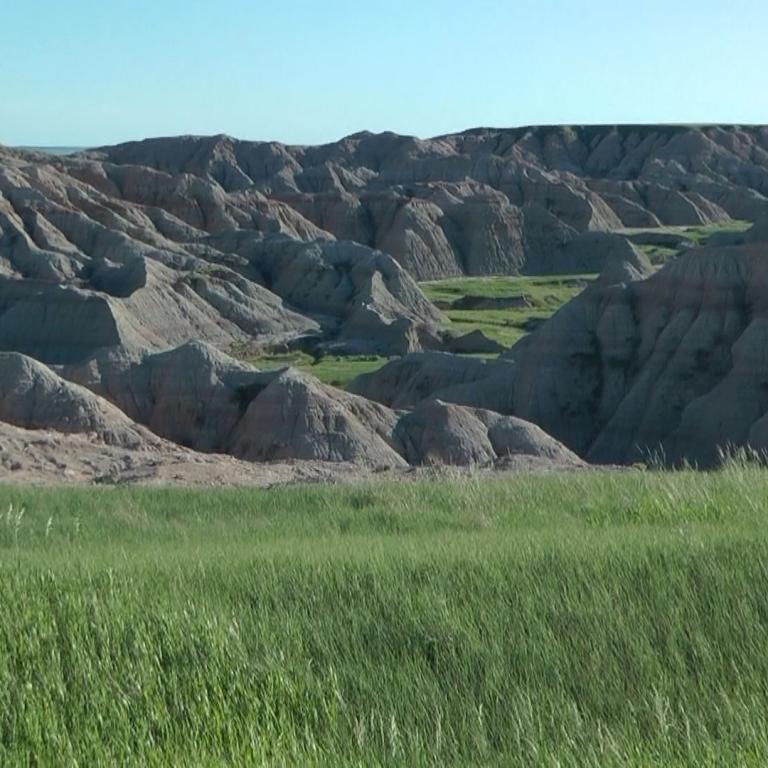 Eine weite Landschaft mit sanften, erodierten Hügeln und einem Vordergrund aus grünem Gras.