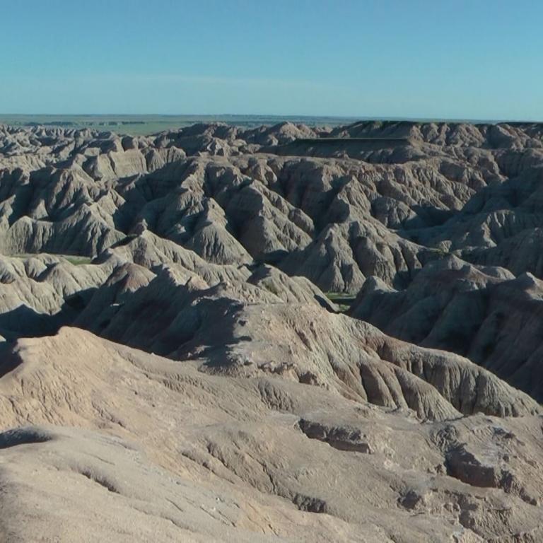 Weitreichende Badlands-Landschaft mit erodierten Felsformationen unter einem blauen Himmel.