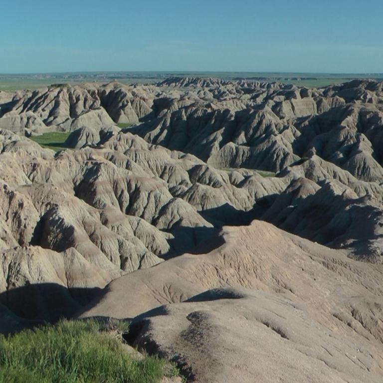 Weite Badlands-Landschaft mit zahlreichen, erodierten Hügeln und einem klaren blauen Himmel.