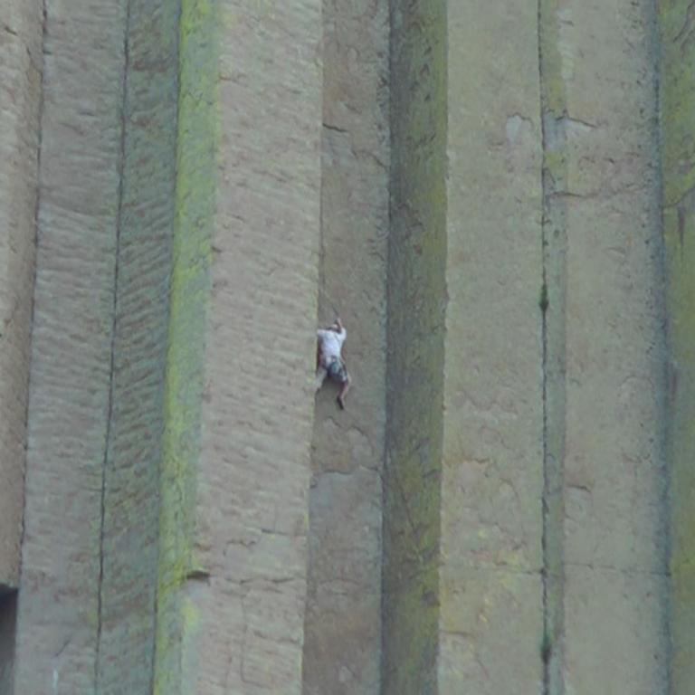 Eine Person klettert an einer massiven Steinwand mit Säulenreihen.