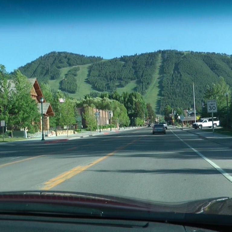 Ein Blick aus einem Auto auf eine Straße, die durch ein Tal führt, mit Chalet-Häusern und bewaldeten Bergen im Hintergrund.