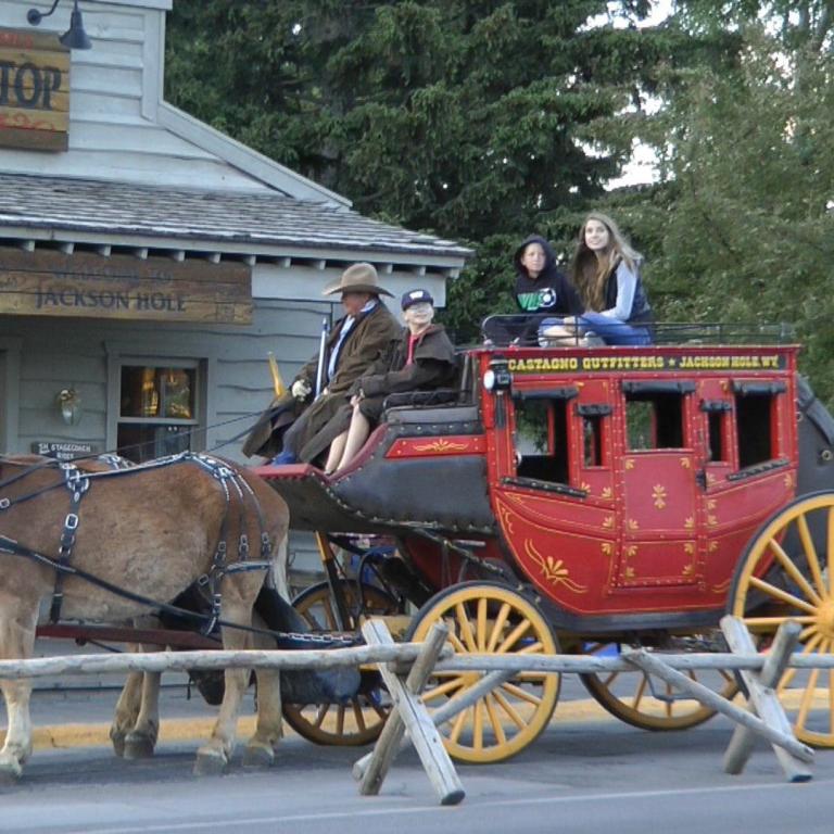 Ein historischer Zug mit roter Kutsche, gezogen von zwei Pferden, vor einem Stage Stop Gebäude in Jackson Hole.
