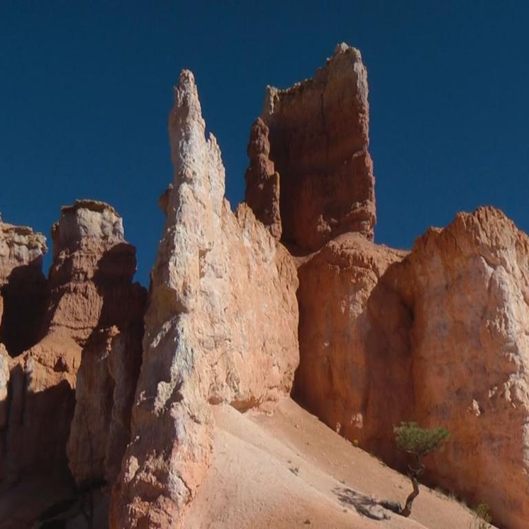Massive, rote Felsformationen und Klippen in einer Wüstenlandschaft unter klarem blauem Himmel.