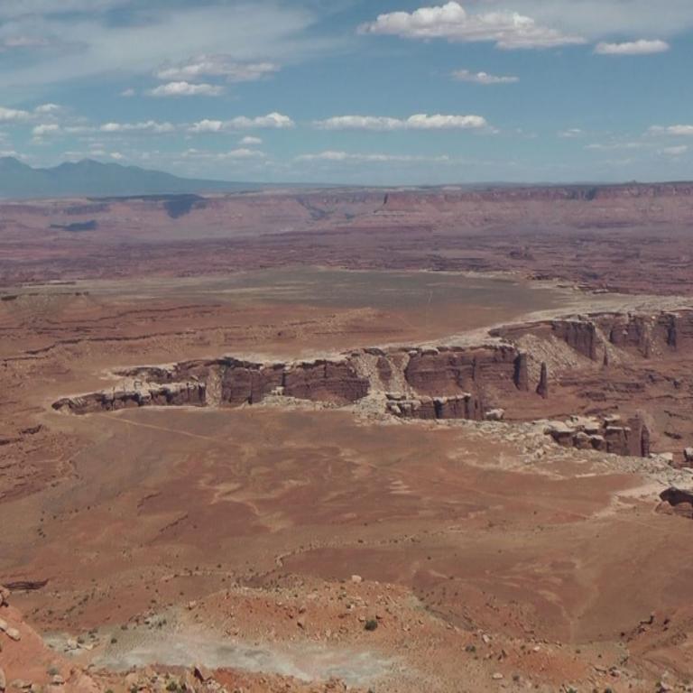 Panoramablick auf eine weite, felsige Wüste mit deutlichen Tafelbergen und einem tiefen Canyon im Hintergrund.