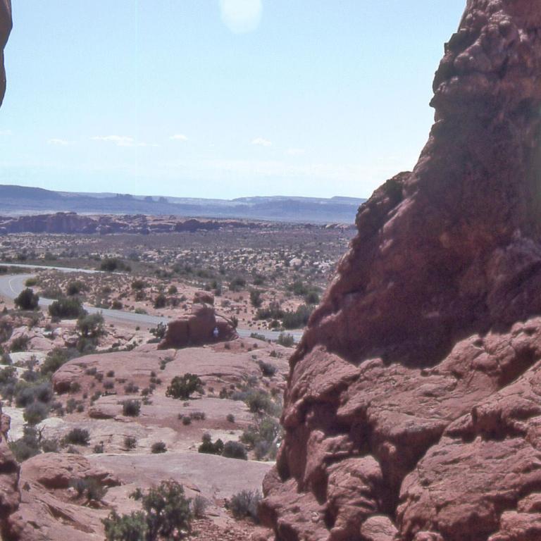 Panoramablick über eine weite, aride Wüstenlandschaft mit rötlichen Felsformationen im Vordergrund.