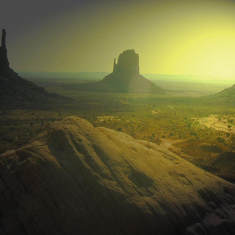 Mehrere große Felsformationen stehen in einer weiten Wüstenlandschaft bei Sonnenuntergang.