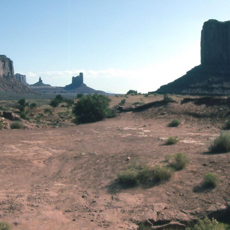 Weite Aufnahme einer ariden Wüstenlandschaft mit markanten, turmartigen Felsformationen im Hintergrund.