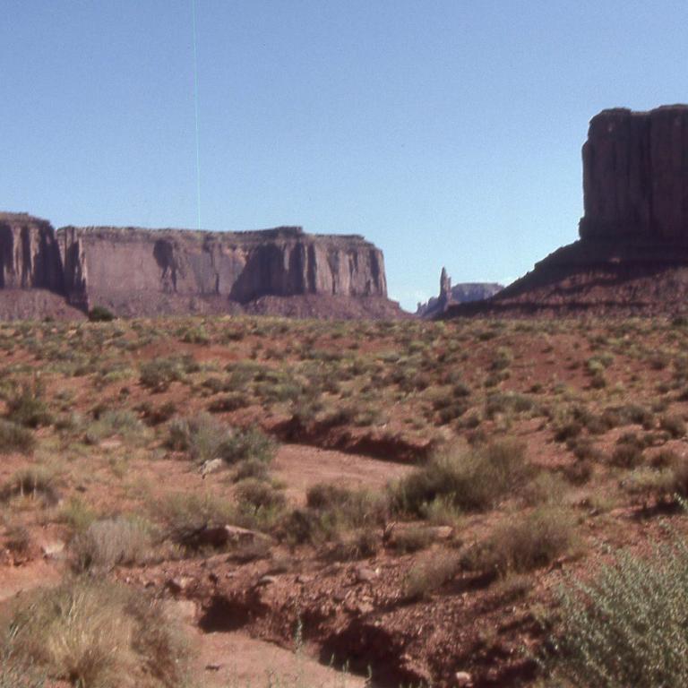 Weite Wüstenlandschaft mit markanten Felsformationen und Buttes unter klarem blauem Himmel.