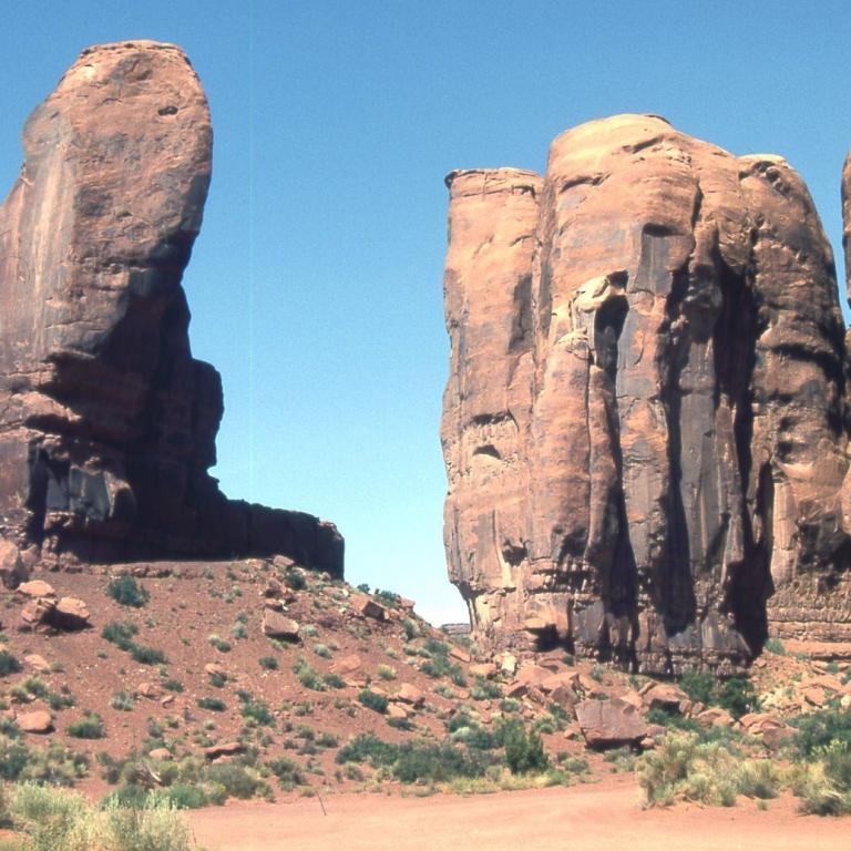 Große, erodierte Sandsteinformationen in einer trockenen Wüstenlandschaft unter blauem Himmel.