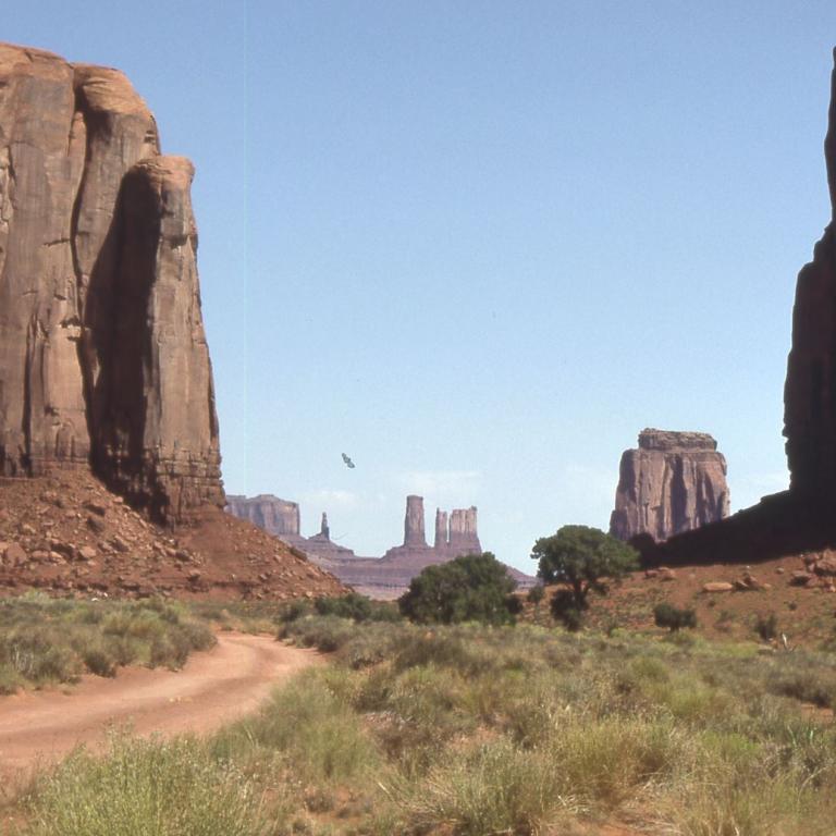 Massive Sandsteinfelsformationen säumen einen staubigen Weg in einer weiten Wüstenlandschaft.